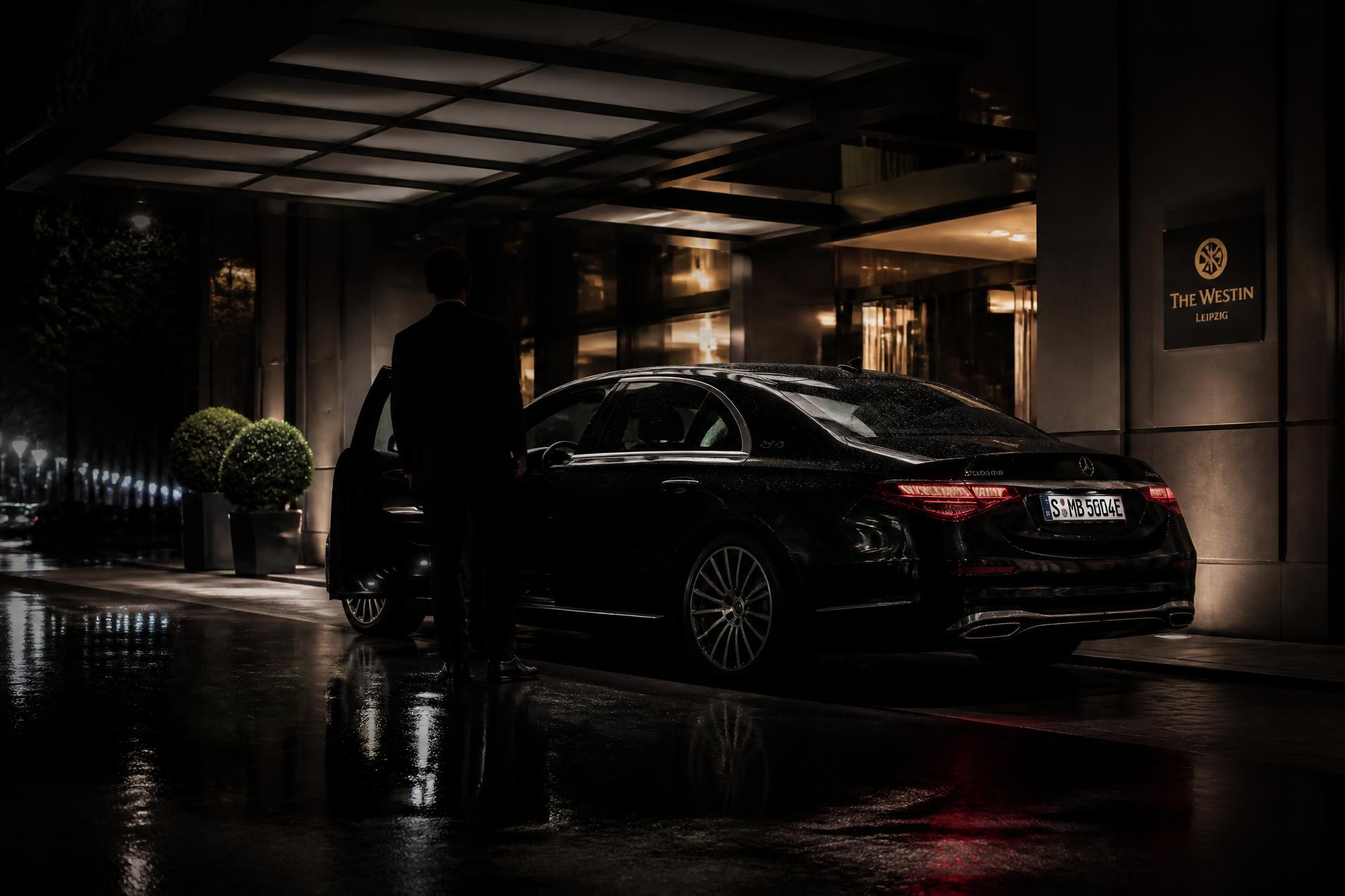 Chauffeur opening the door of a black executive sedan outside a hotel at night